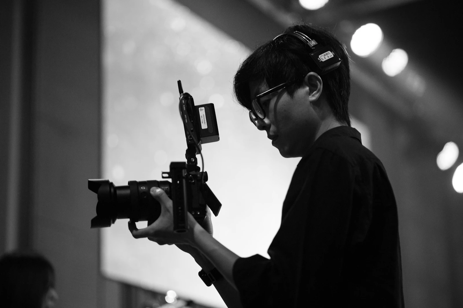 Black-and-white photo of a camera operator wearing an intercom headset, holding a rigged mirrorless camera with a wireless video transmitter